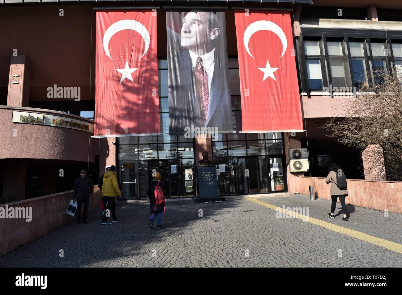 18 March 2019, Turkey, Ankara: People walk towards the National Library building as a portrait of Mustafa Kemal Ataturk, modern Turkey's founding president, and Turkish national flags are hanged on the occasion of the 104th anniversary of the Canakkale Victory. Photo: Altan Gocher | usage worldwide Stock Photo