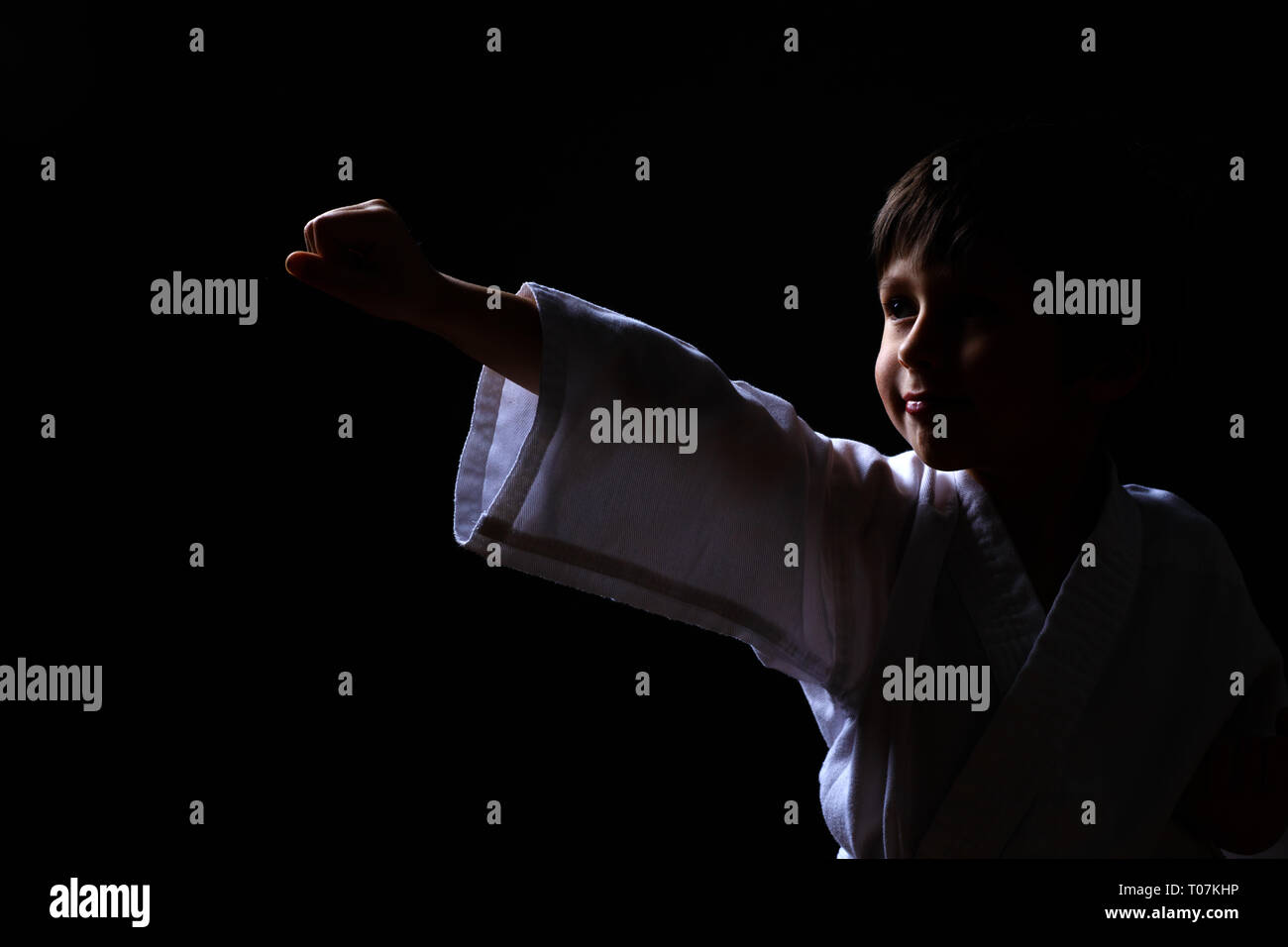 Karate boy in white kimono posing on dark background. Child ready for martial arts fight. Kid fighting at Aikido training. Best for martial fights and Stock Photo