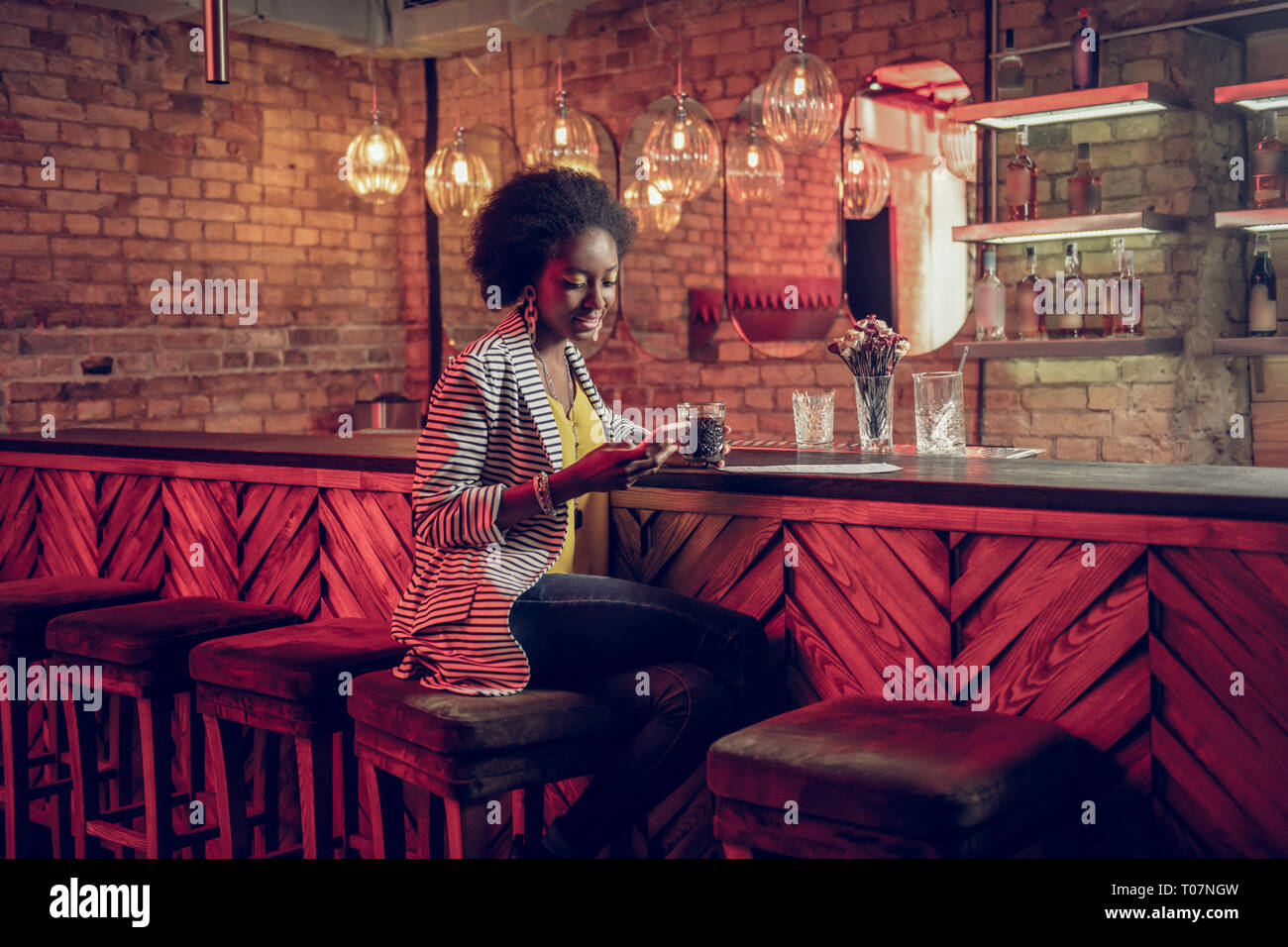 Ravishing gorgeous African-American female checking phone while holding drink Stock Photo