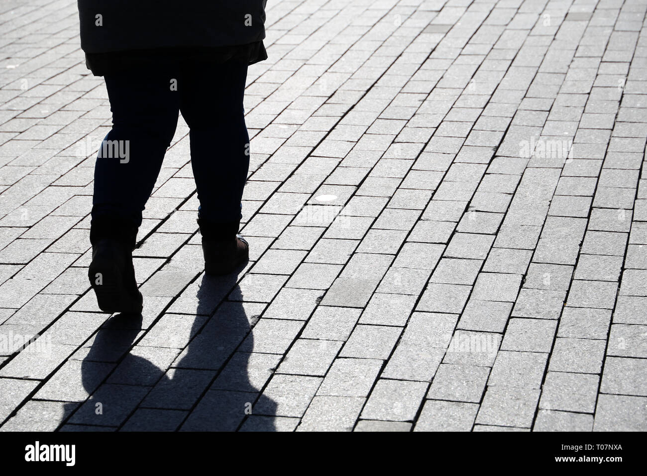 Silhouette of fat woman walking down the street, black shadow on pavement. Thick legs in jeans, concept of overweight, diet, loneliness, dramatic life Stock Photo