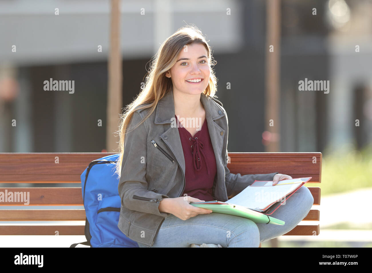 Happy student looking at camera sitting on a bench in a park Stock Photo