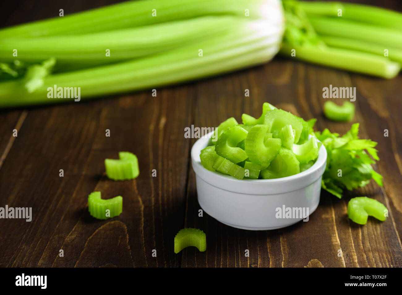 Cutted celery sticks in white ceramic bowl on wooden background Stock Photo