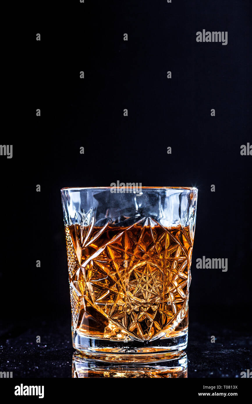 Drinking glass with whiskey on black background. Golden bourbon alcohol drink on table with copy space Stock Photo