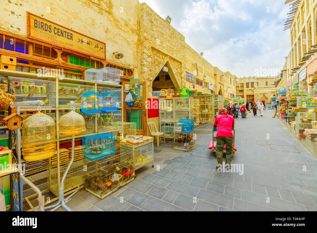 Doha, Qatar - February 19, 2019: a porter with cart walks along pedestrian street of Bird Souq Market, full of cages with birds and pets in Doha Stock Photo