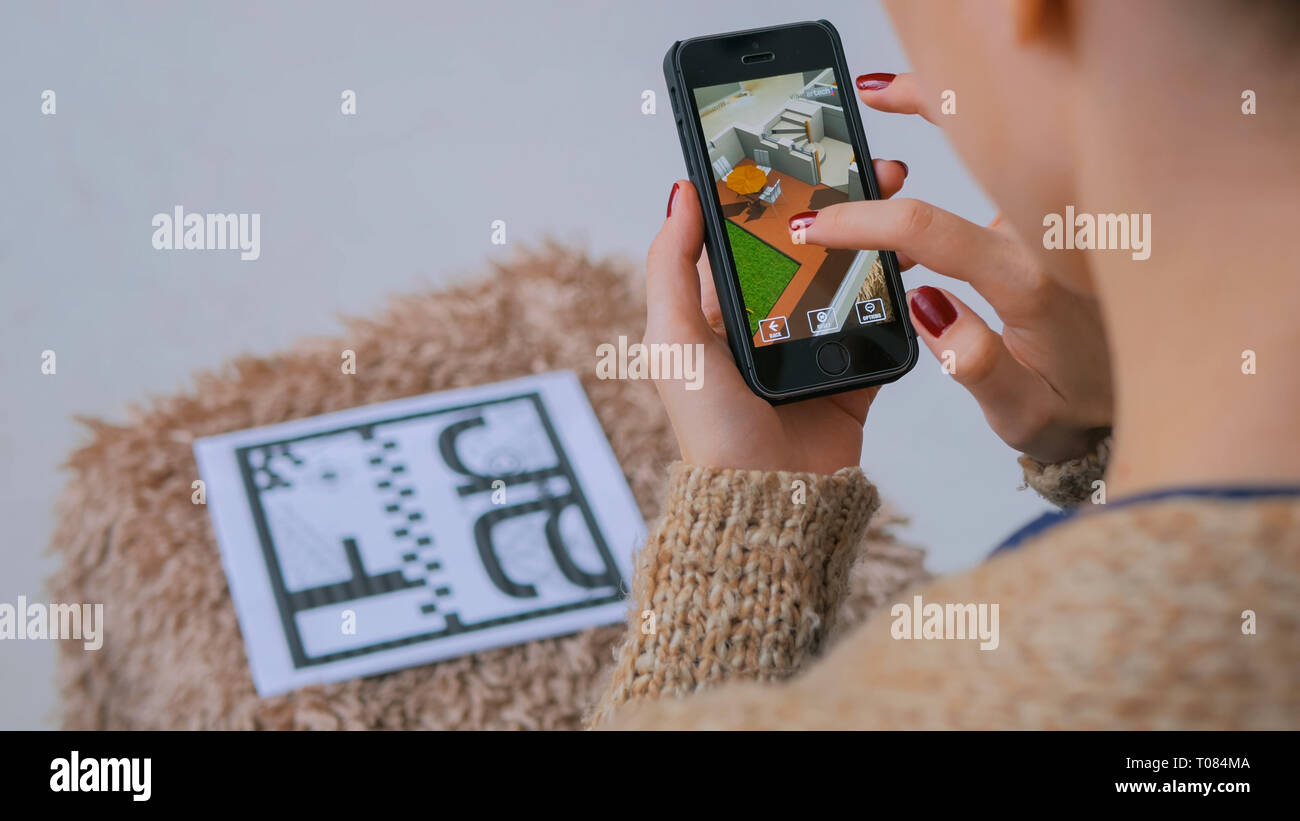 Woman using smartphone with augmented reality app, checking virtual house plan Stock Photo
