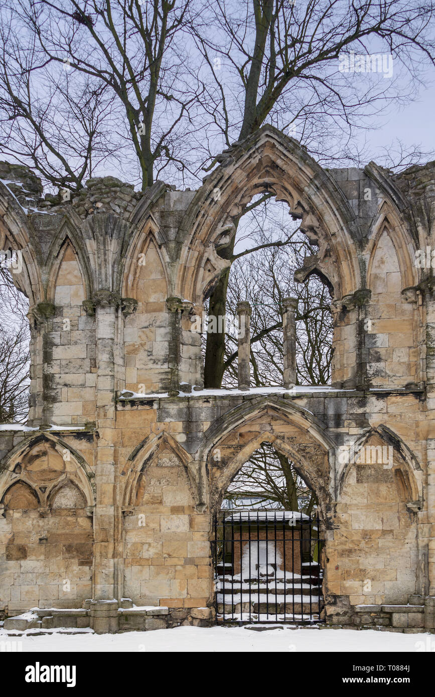 A view through an arched gate in the ruins of St Mary’s Abbey in York.  Snow lies on the ground and winter trees are in the background. Stock Photo
