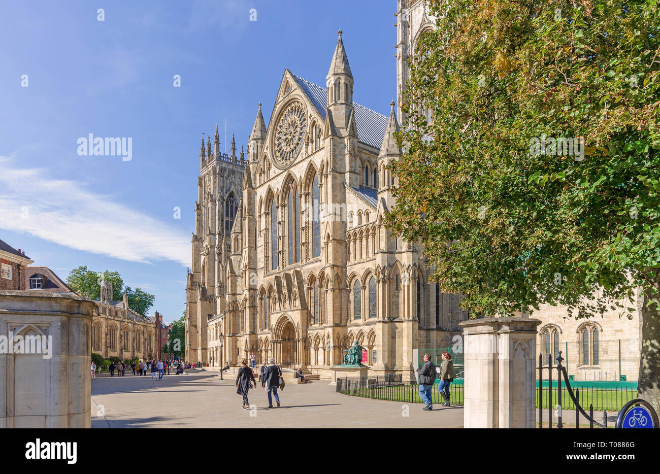 The South facing York Minster and environs.  There is a church opposite and tourists mill about, There is a blue sky above. Stock Photo