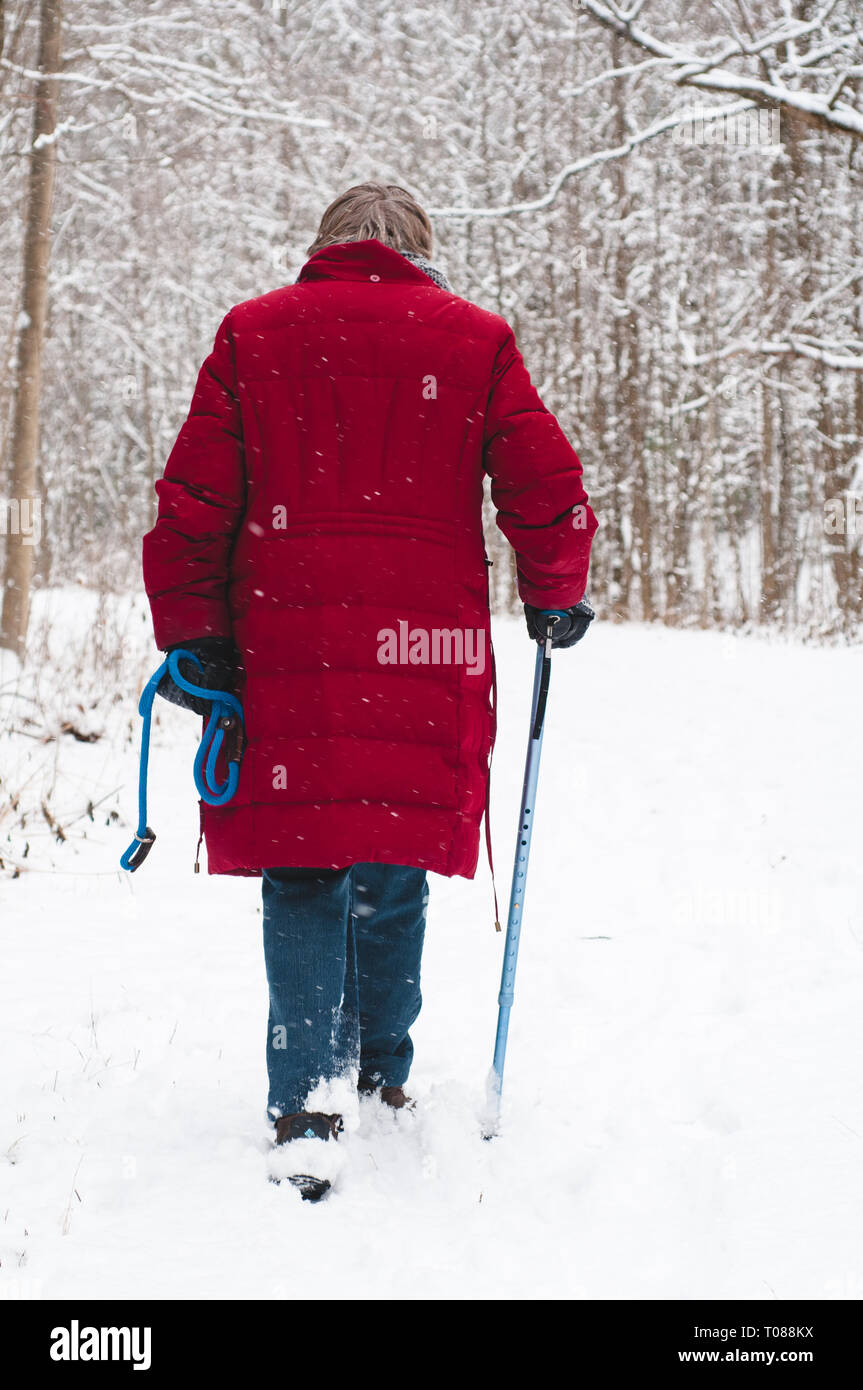 Senior woman walking down a snowy forest trail in the winter Stock Photo