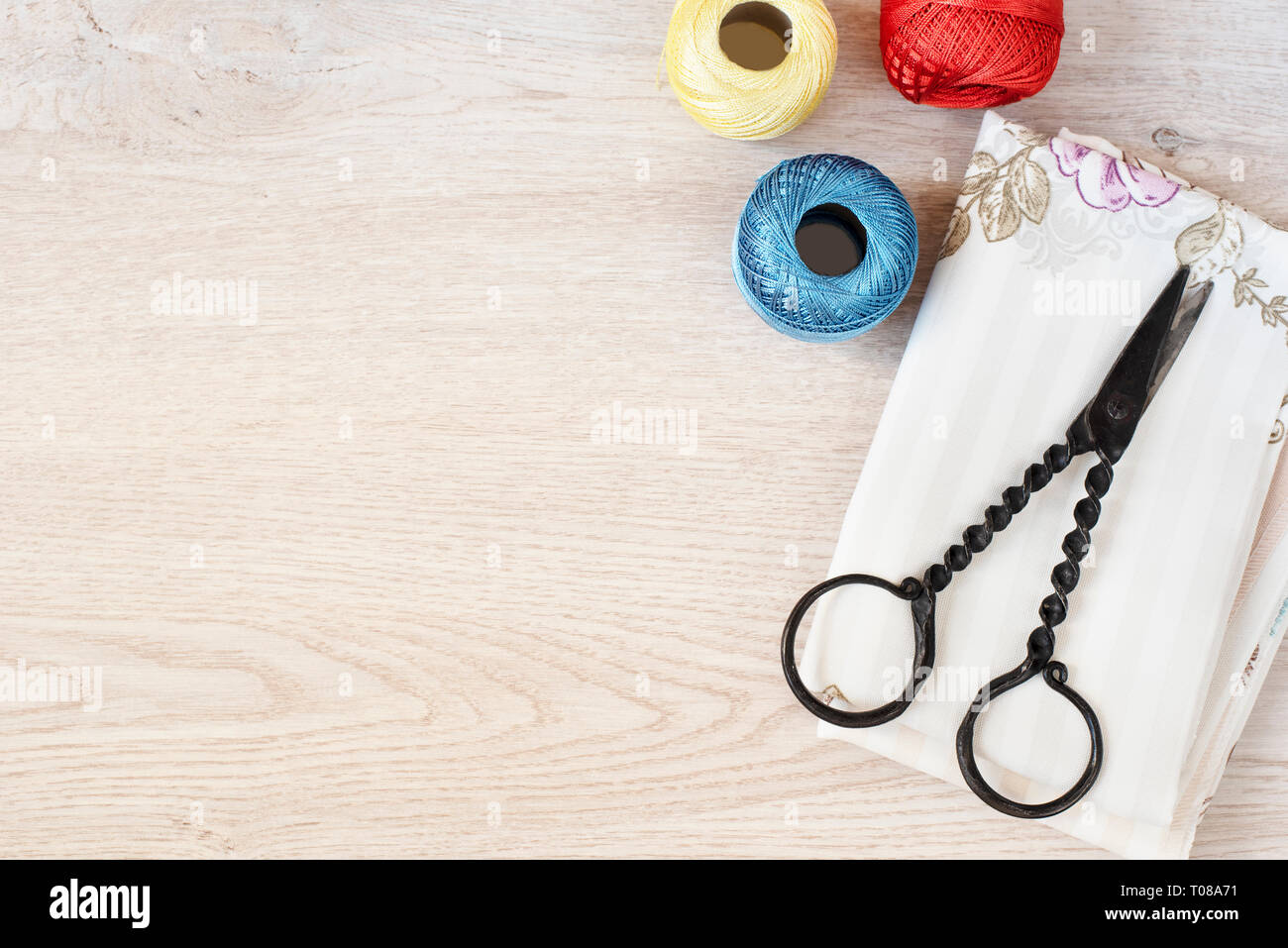 Composition with sewing, knitting threads, fabrics and antique scissors on gray wooden background, top view Stock Photo