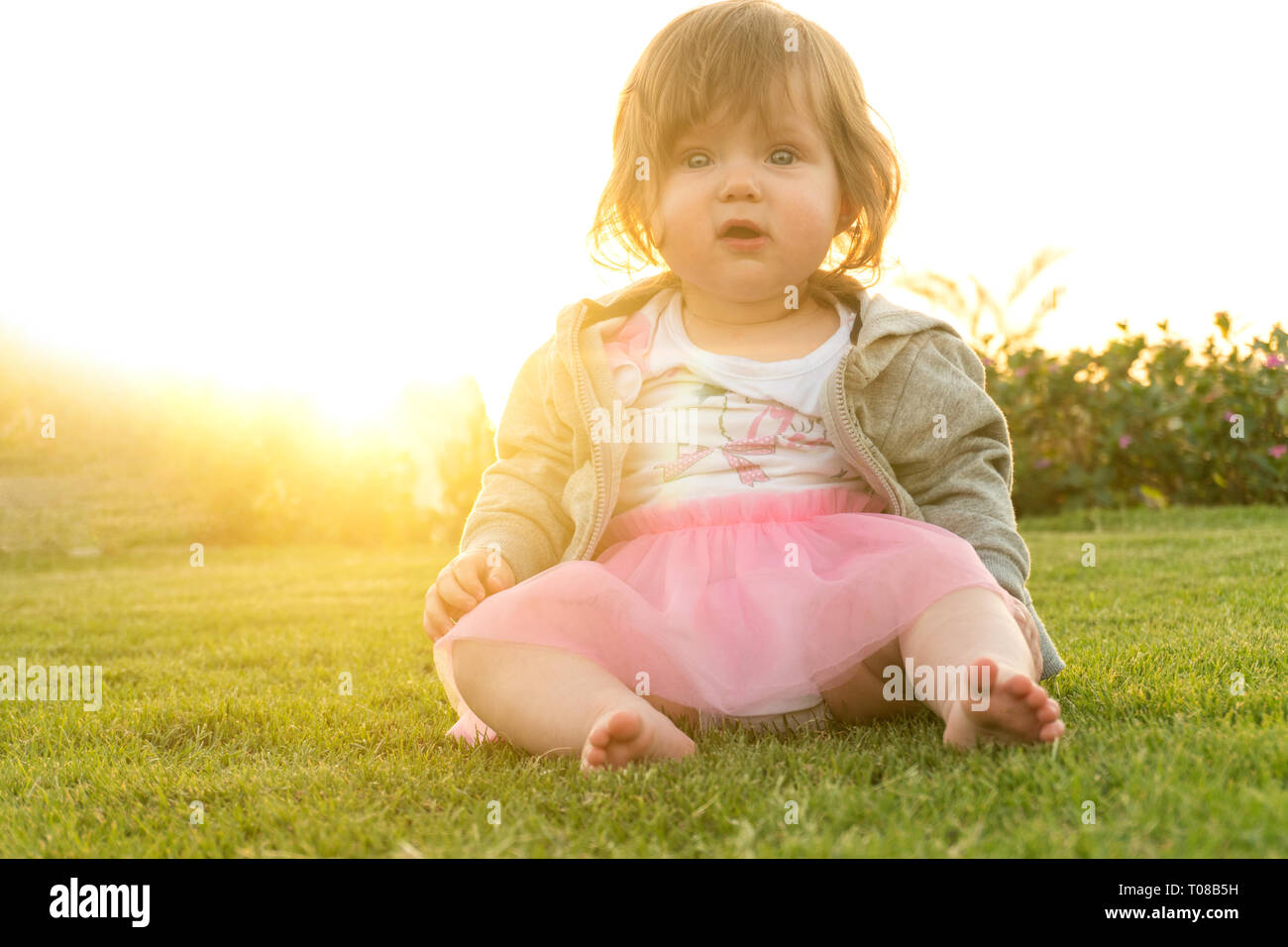 Funny girl sitting on grass on sunset Stock Photo