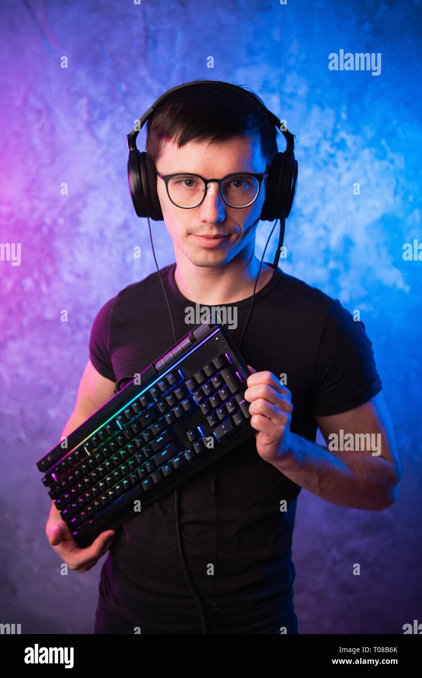 Computer nerd with keyboard over colorful pink and blue neon lit wall Stock Photo