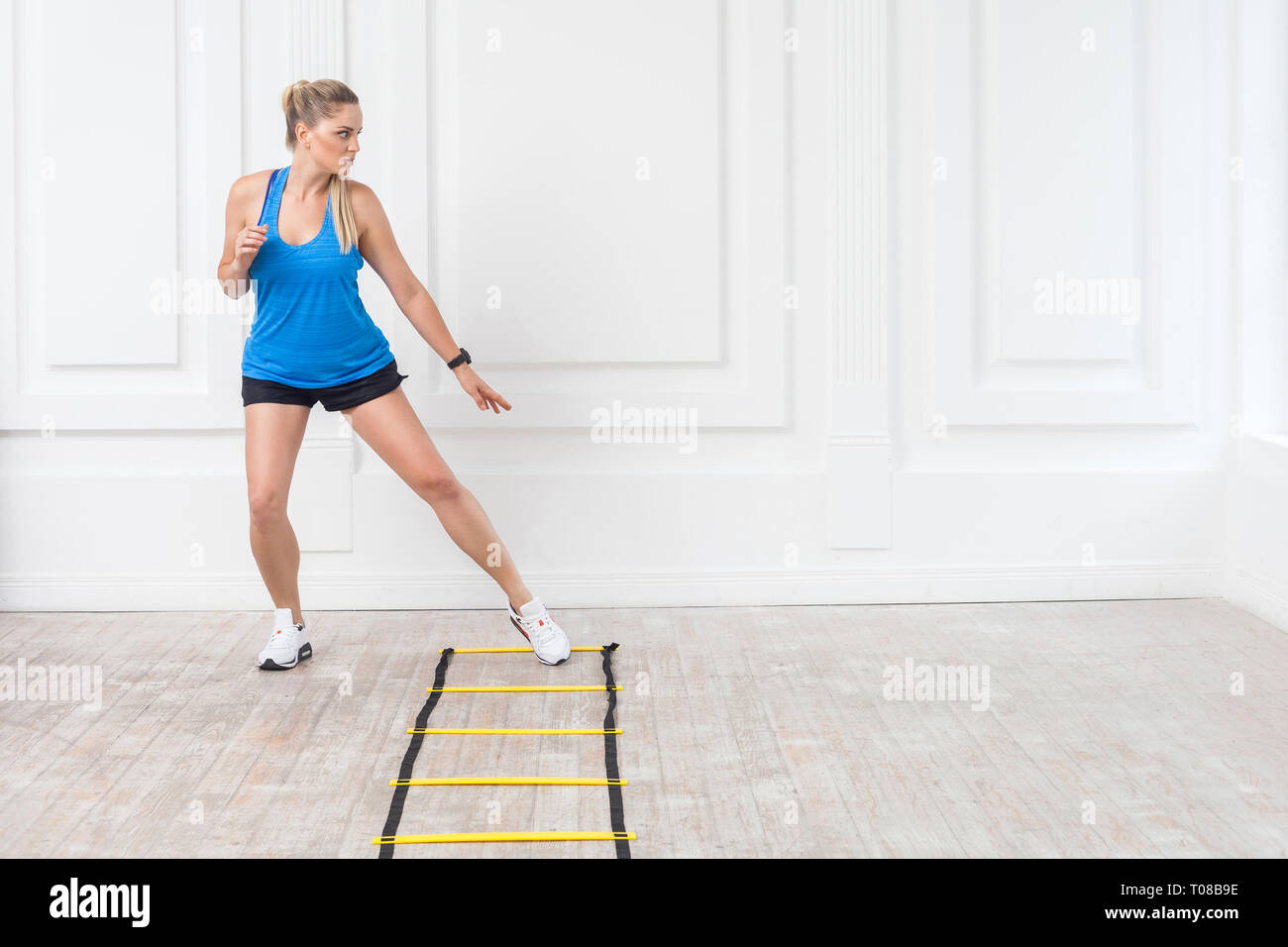 Full length of sporty beautiful young athletic blonde woman in black shorts and blue top are cardio workout with speed straps on floor and training on Stock Photo