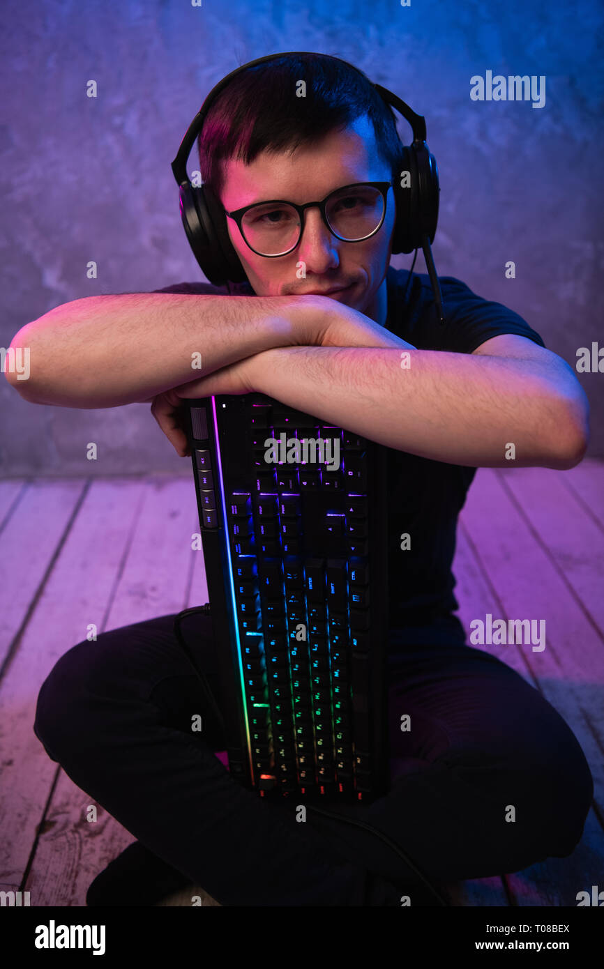 Portrait of the young handsome pro gamer sitting on the floor with keyboard in neon colored room Stock Photo