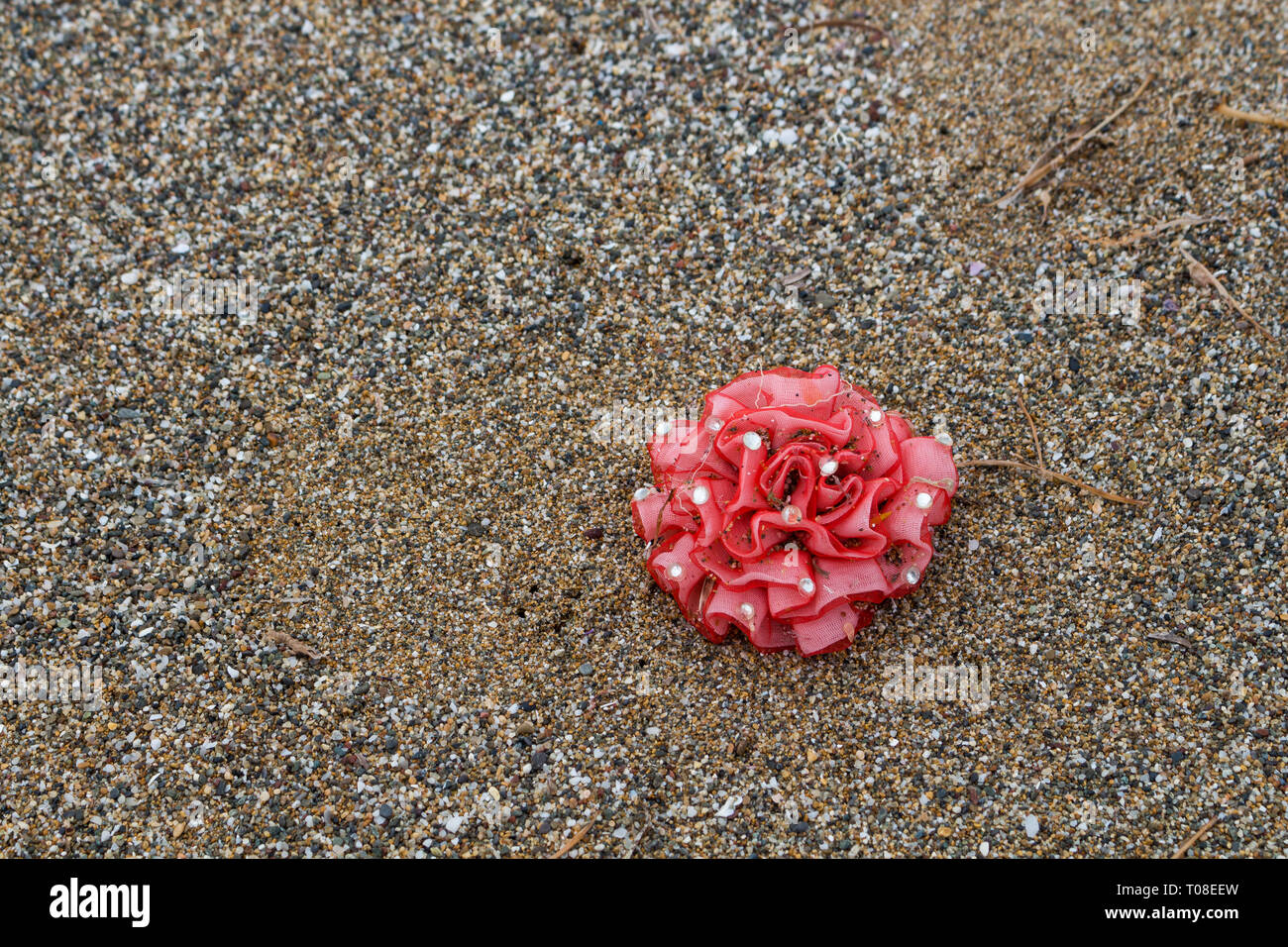 Red flower on the leastic hair bands, forgotten or lost on the beach.  Part of the set Beach discoveries. Crete, Greece. Stock Photo