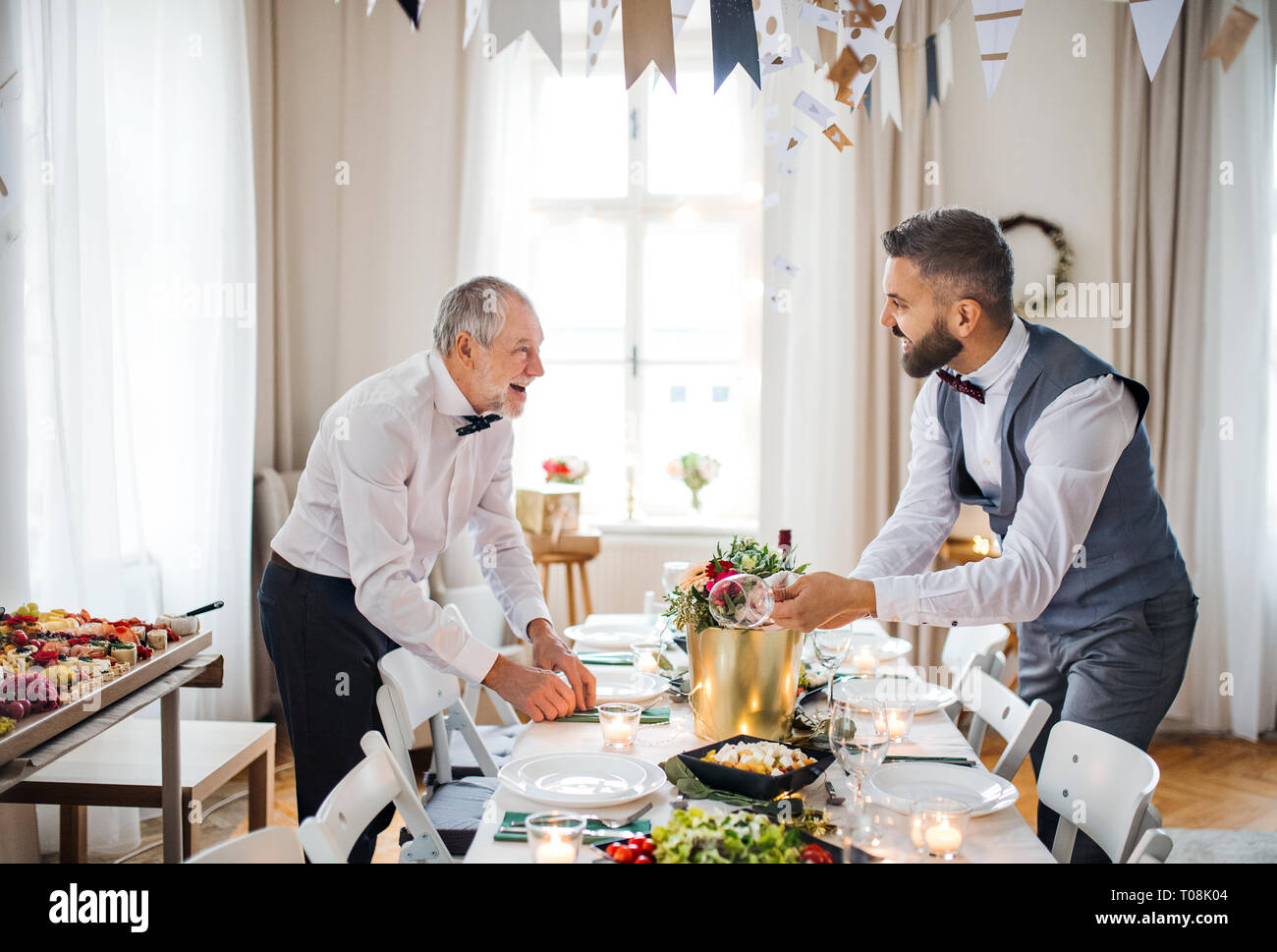 Two men with bows setting a table for an indoor party, talking. Stock Photo