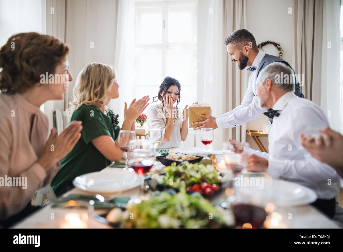 A man giving gift to a young surprised woman on a family birthday party. Stock Photo