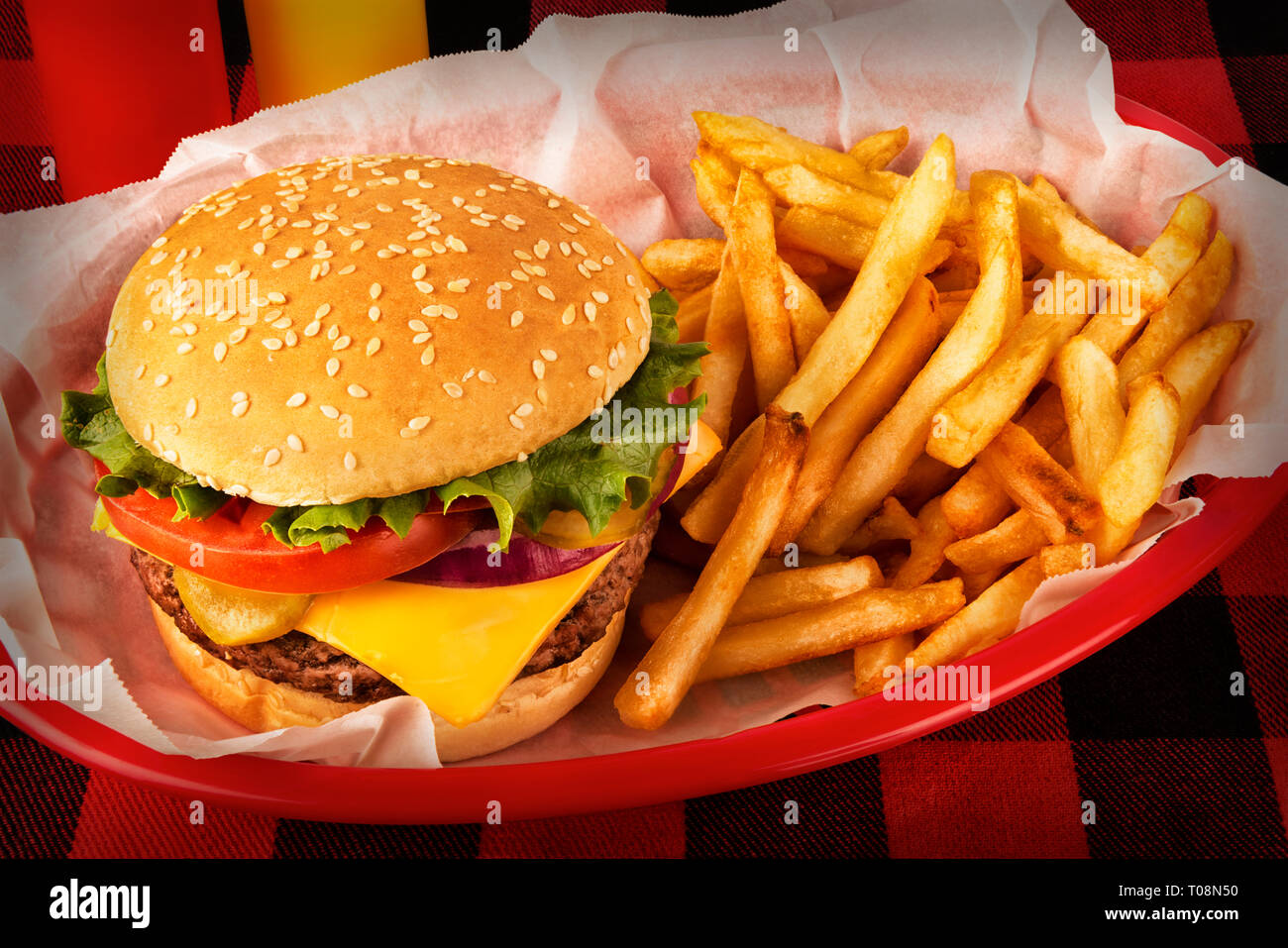 Burger and french fries in basket on tartan tablecloth. Ketchup and mustard bottle in background. Close up. Stock Photo