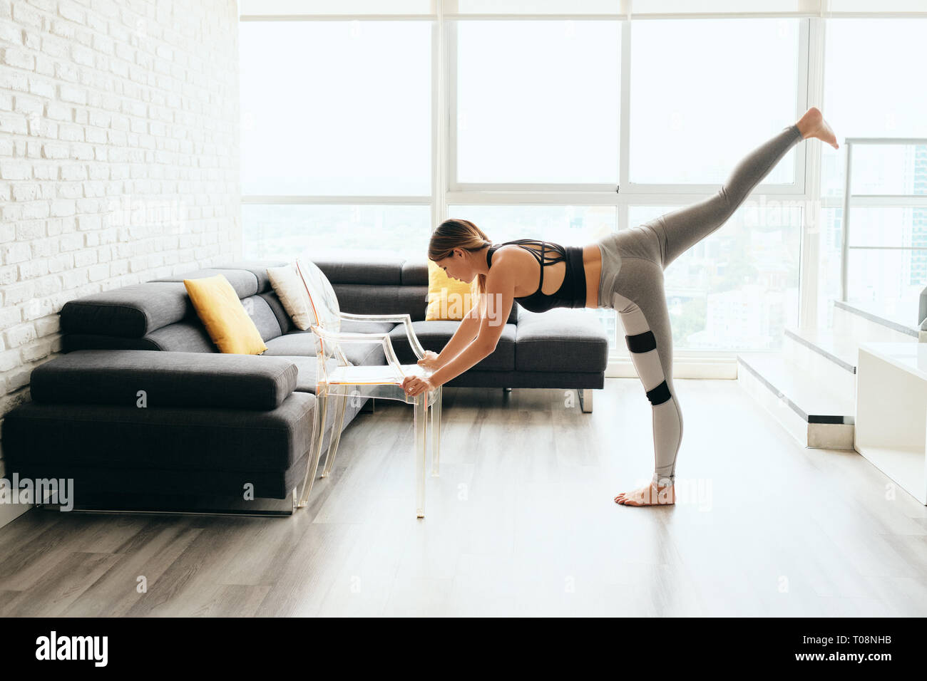 Adult Woman Training Body By Raising Legs Using Chair Stock Photo