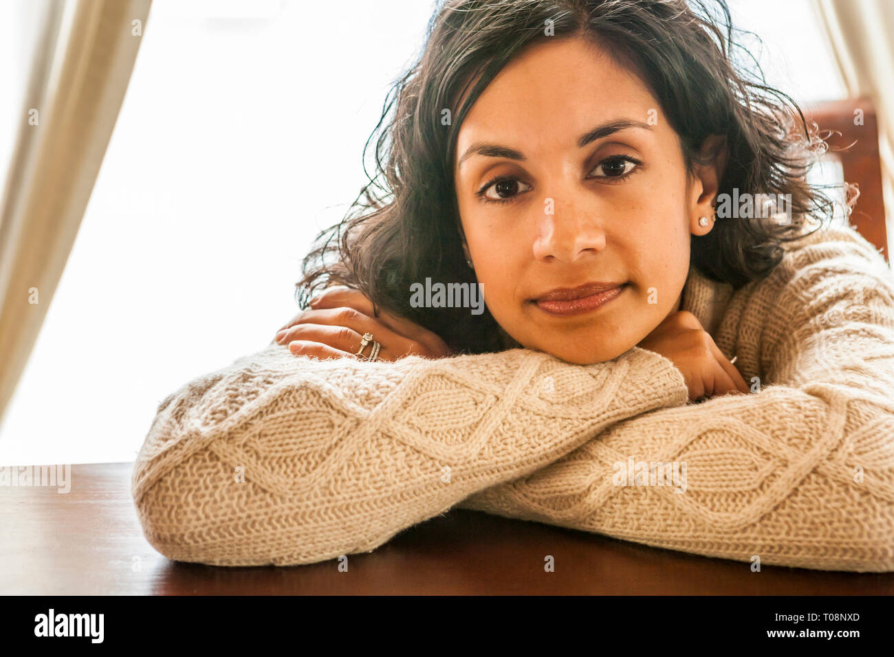 A portrait of an early 30's Sri Lanken - American woman leaning on a table and resting her head on her arms. Stock Photo