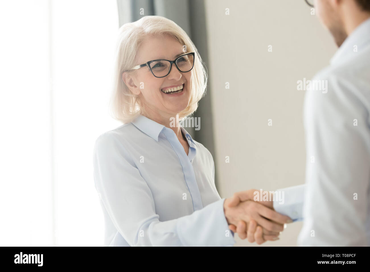 Happy mature businesswoman handshaking partner client, trust and gratitude handshake Stock Photo