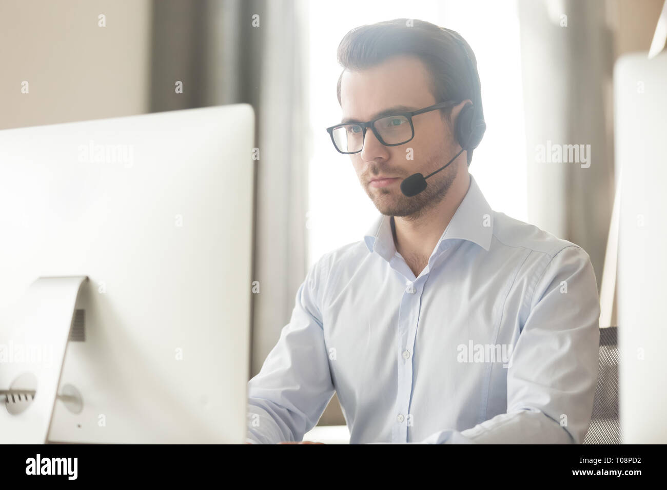 Serious businessman talking with headset on computer making conference call Stock Photo