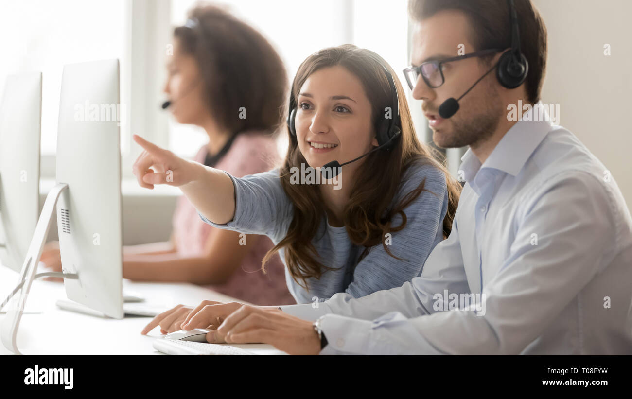 Female call center agent helping male colleague pointing at computer Stock Photo