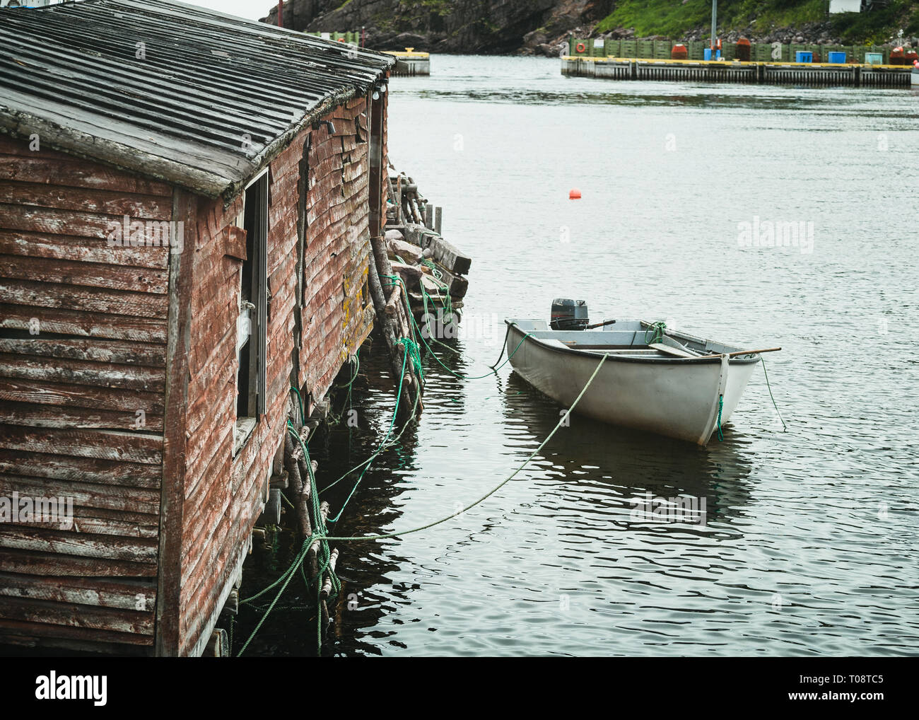 Small fishing boat tied up to a fishing shed in a safe harbor along the coast of Newfoundland, Canada. Stock Photo