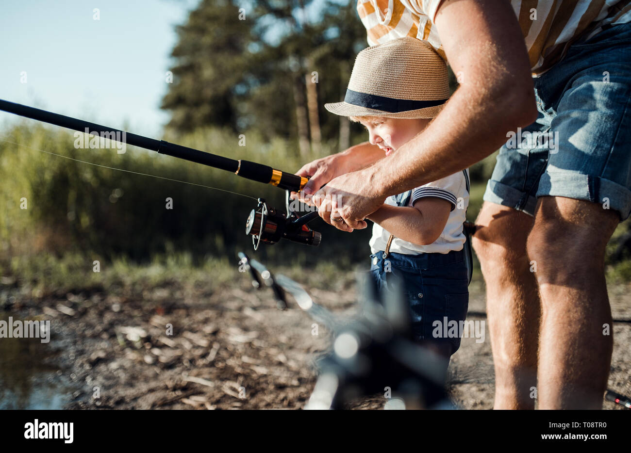 A midsection of father with small toddler boy fishing by a lake. Stock Photo