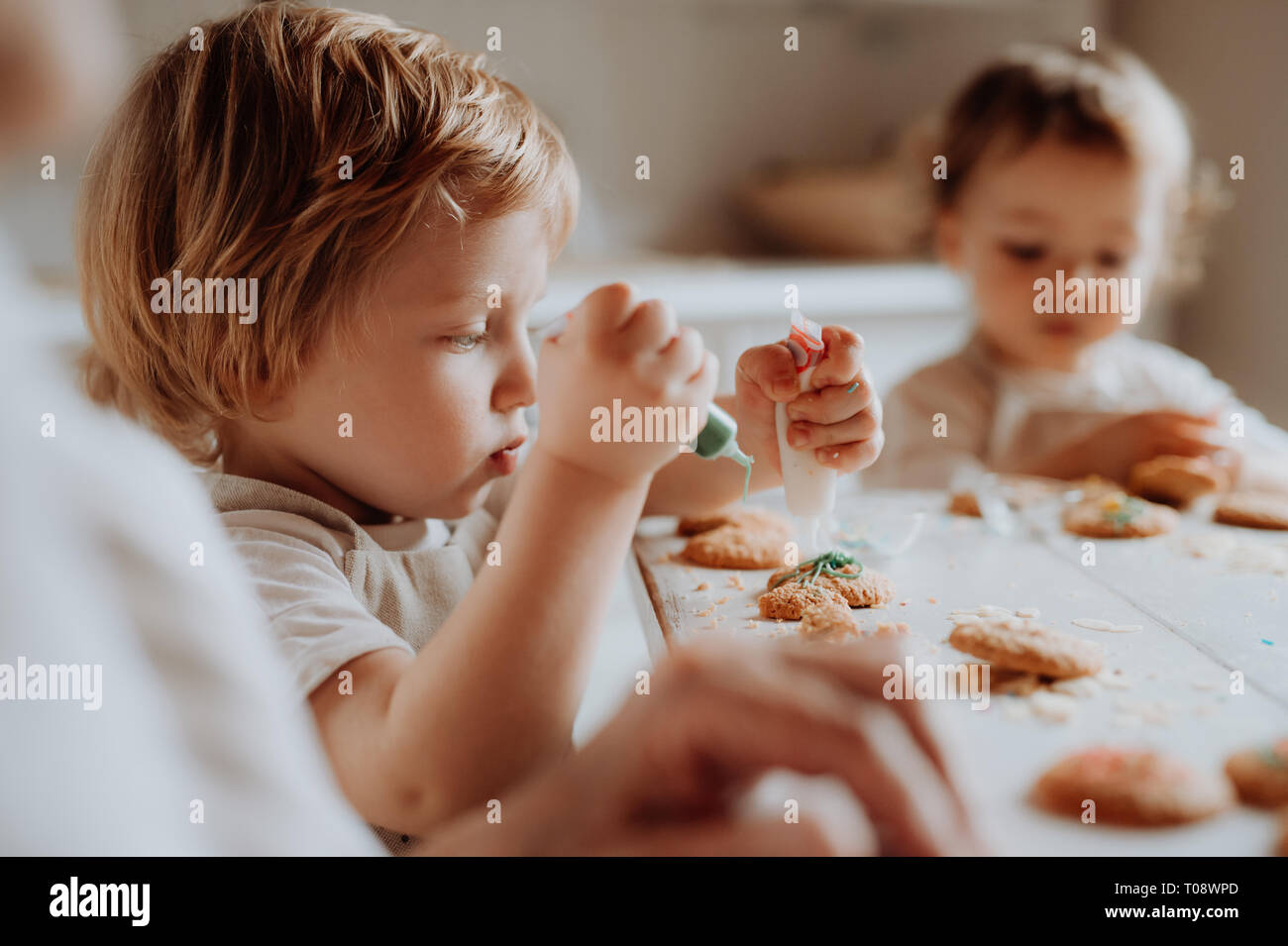 Two small toddler children sitting at the table, decorating and eating cakes at home. Stock Photo