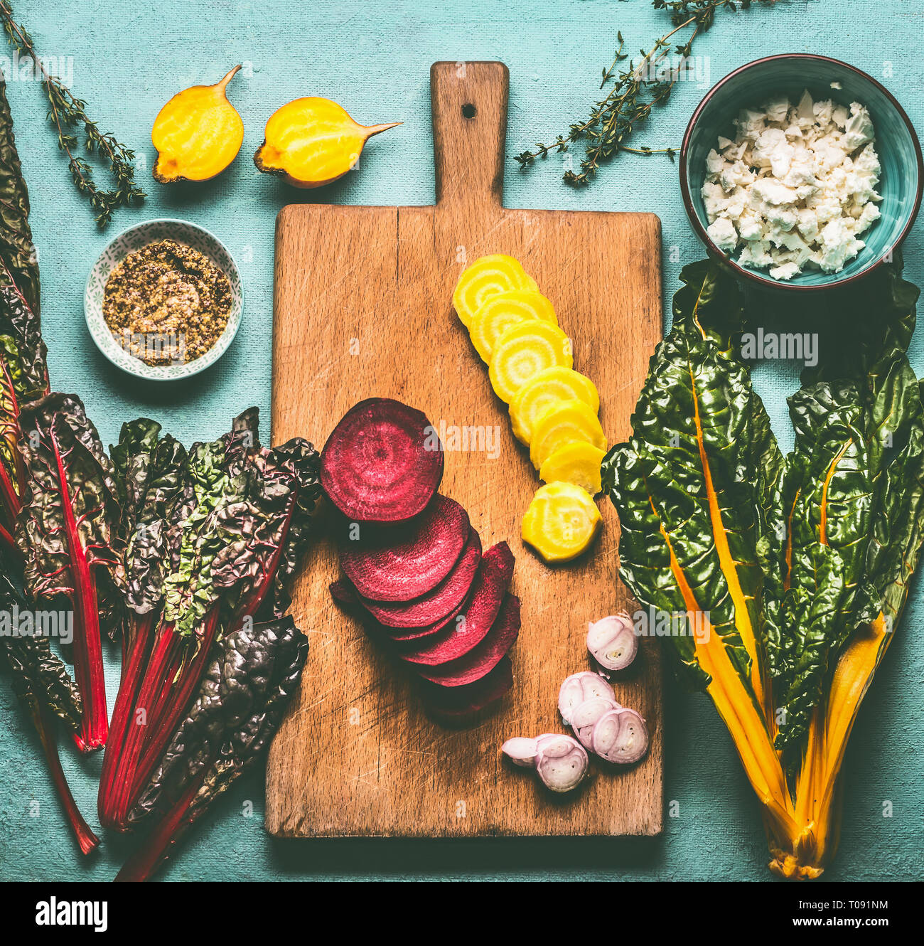 Colorful sliced beetroots with greens ingredients on kitchen table with cutting board, top view. Healthy vegetarian eating and cooking Stock Photo