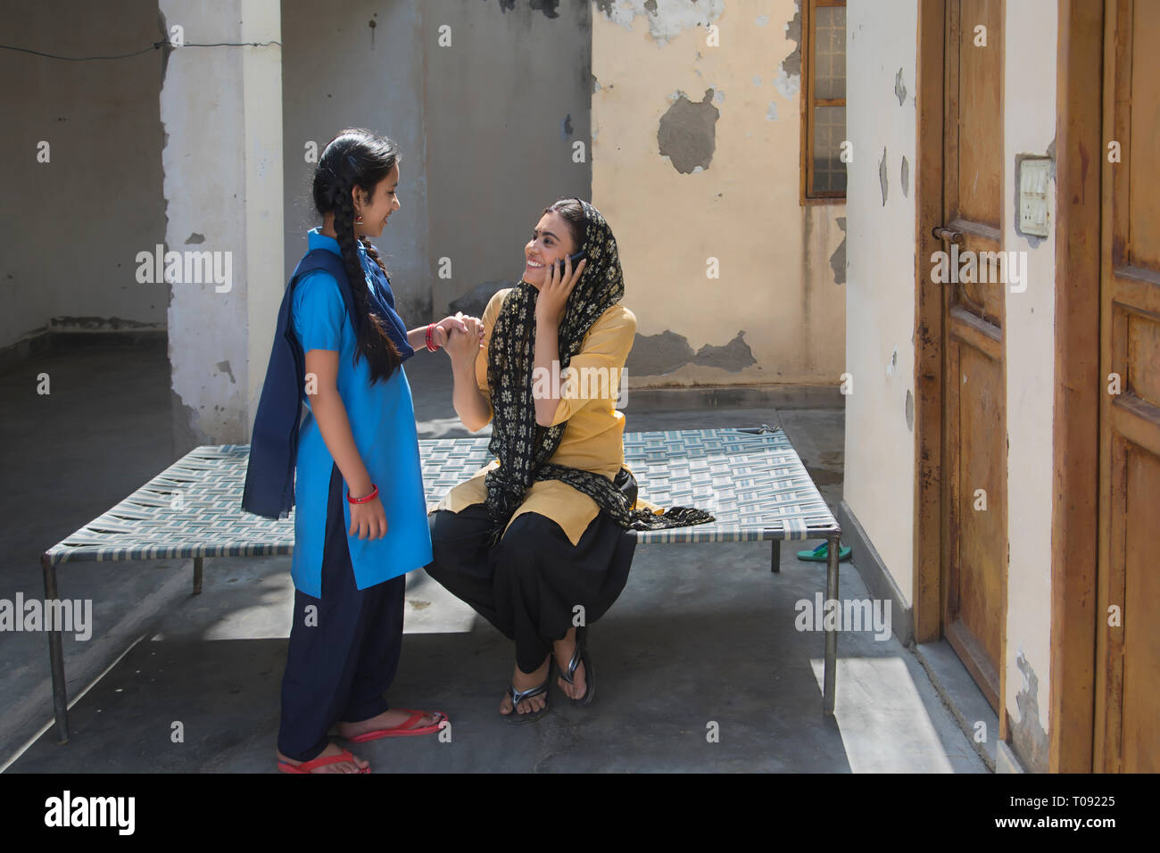 Happy village woman sitting on a cot talking over mobile phone holding