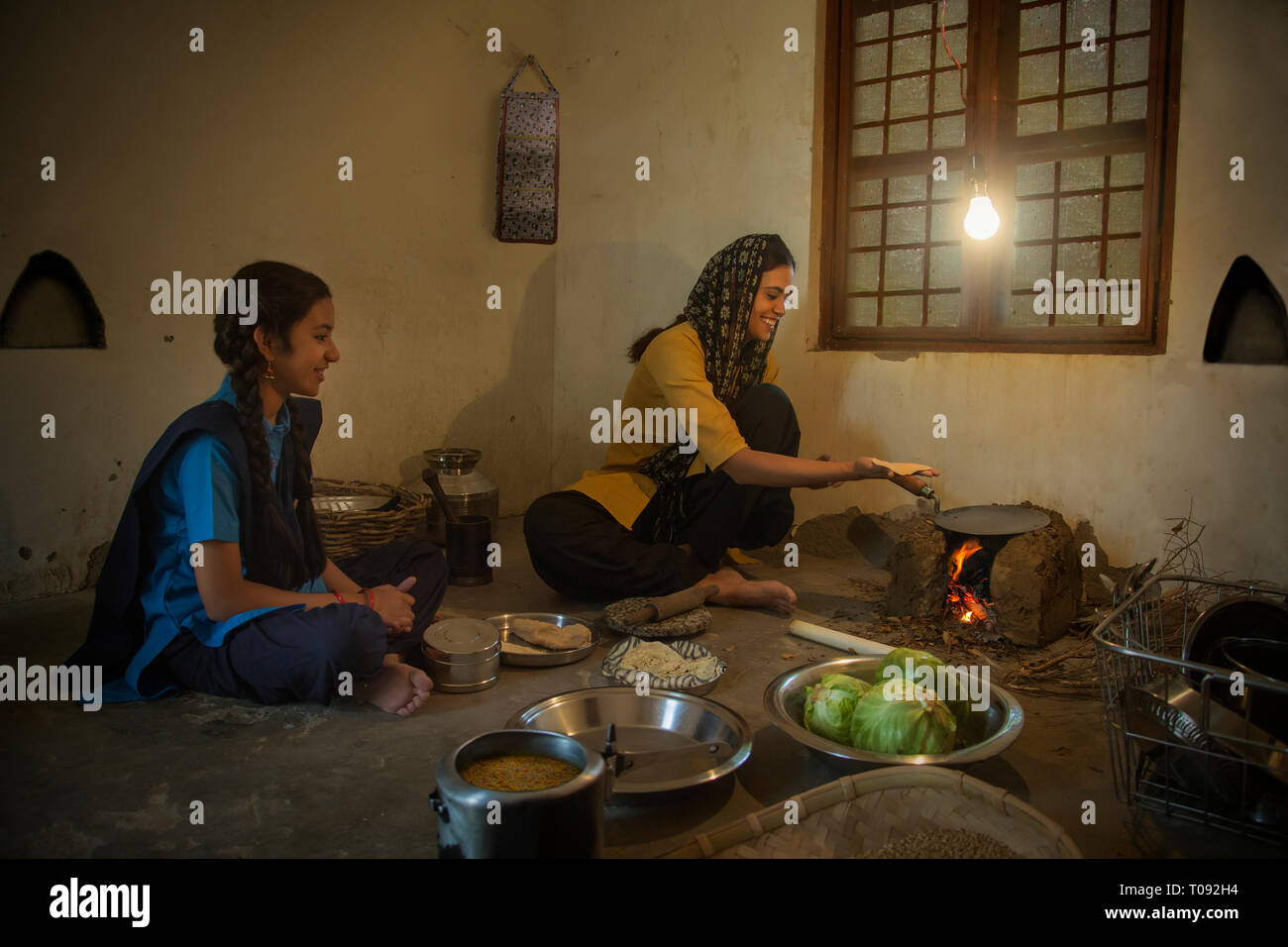 Rural woman sitting in kitchen cooking food on firewood with utensils ...