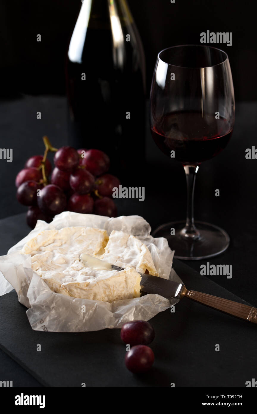 Bottle and glass of wine with cluster of grapes, rustic bread, brie cheese, antique knife Stock Photo