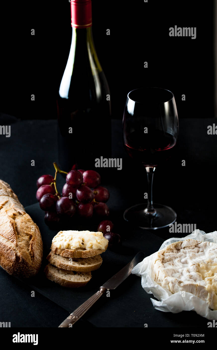 Bottle and glass of wine with cluster of grapes, rustic bread, brie cheese, antique knife Stock Photo