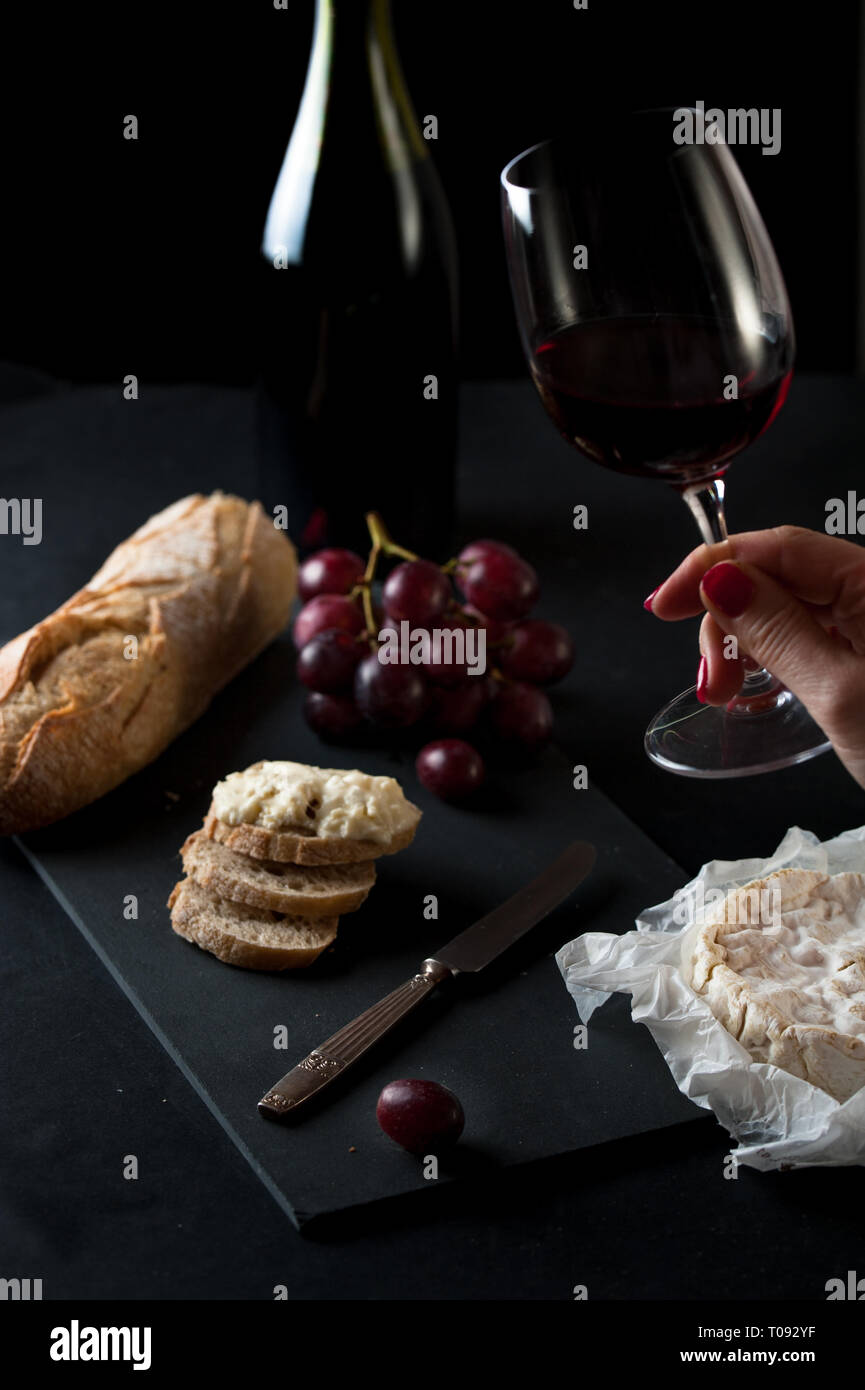 Bottle and glass of wine with cluster of grapes, rustic bread, brie cheese, antique knife Stock Photo