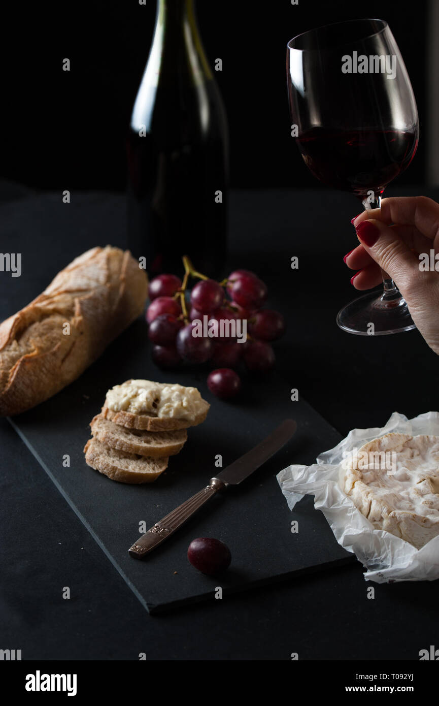 Bottle and glass of wine with cluster of grapes, rustic bread, brie cheese, antique knife Stock Photo
