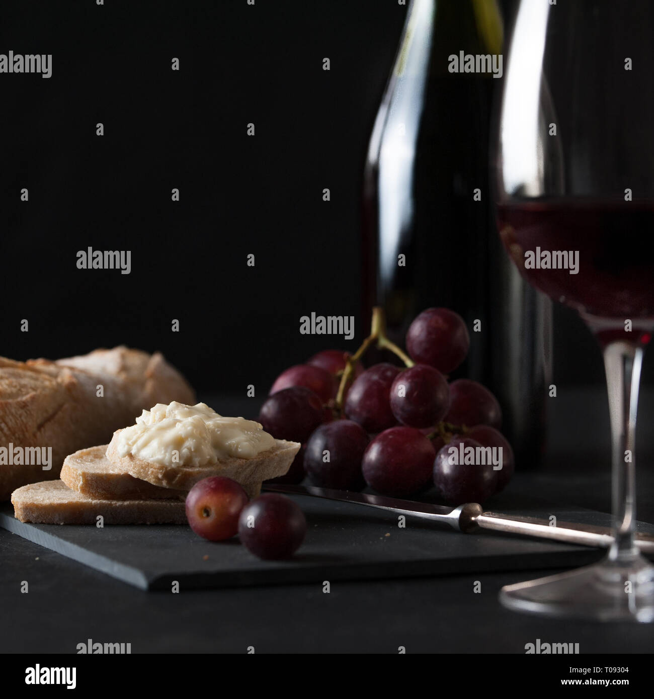 Bottle and glass of wine with cluster of grapes, rustic bread, brie cheese, antique knife Stock Photo