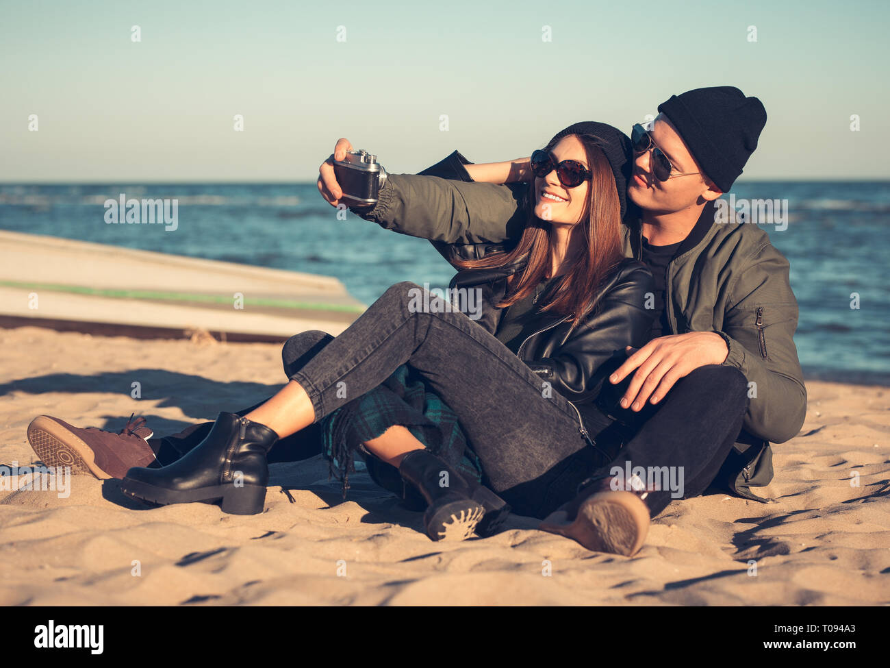 A young loving couple spends fun time by the sea and makes selfies. Man and woman have spring clothes Stock Photo