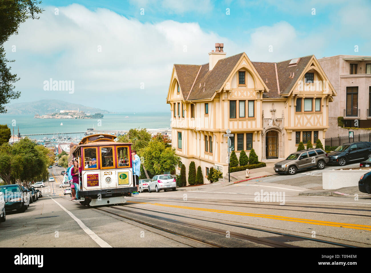 Powell-Hyde cable car climbing up steep hill in central San Francisco with famous Alcatraz Island in the background on a sunny day with blue sky, USA Stock Photo
