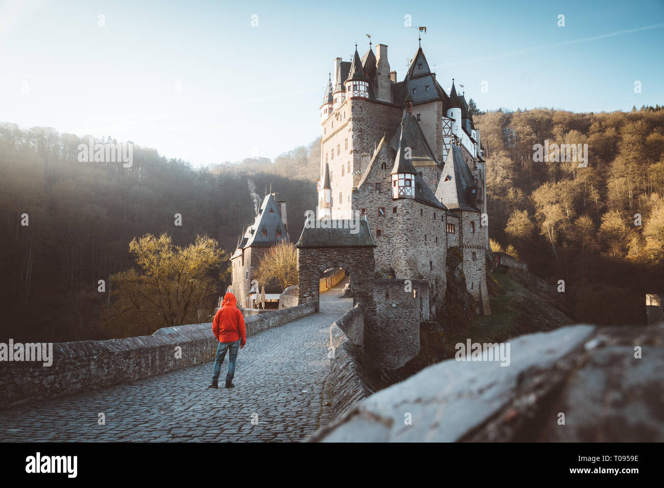 Panorama view of young explorer with backpack taking in the view at famous Eltz Castle at sunrise in fall, Rheinland-Pfalz, Germany Stock Photo