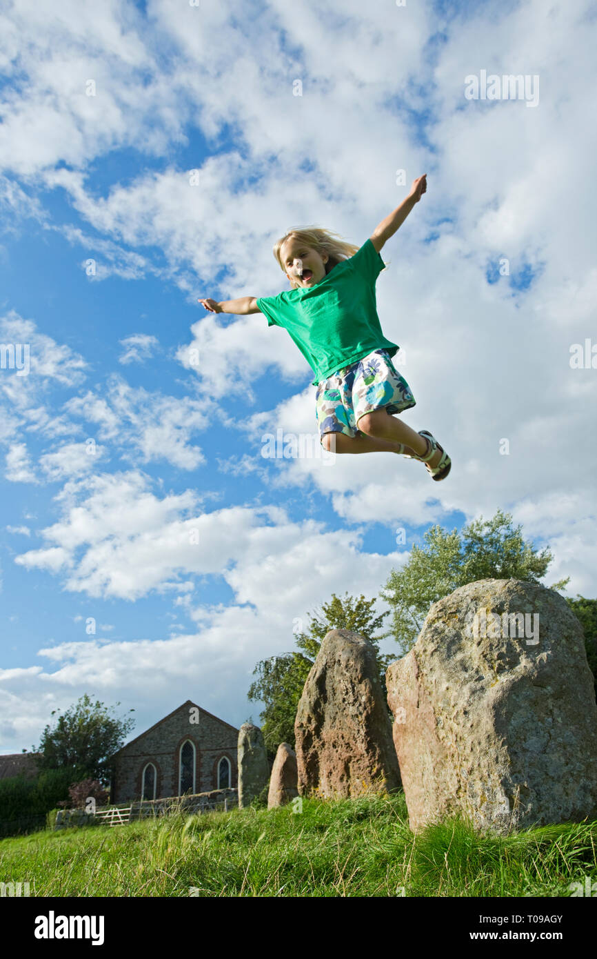 Europe, UK, England, Wiltshire, Avebury Circle. Young girl using levitation power above an ancient stone alignment with Christian church behind. MR. Stock Photo