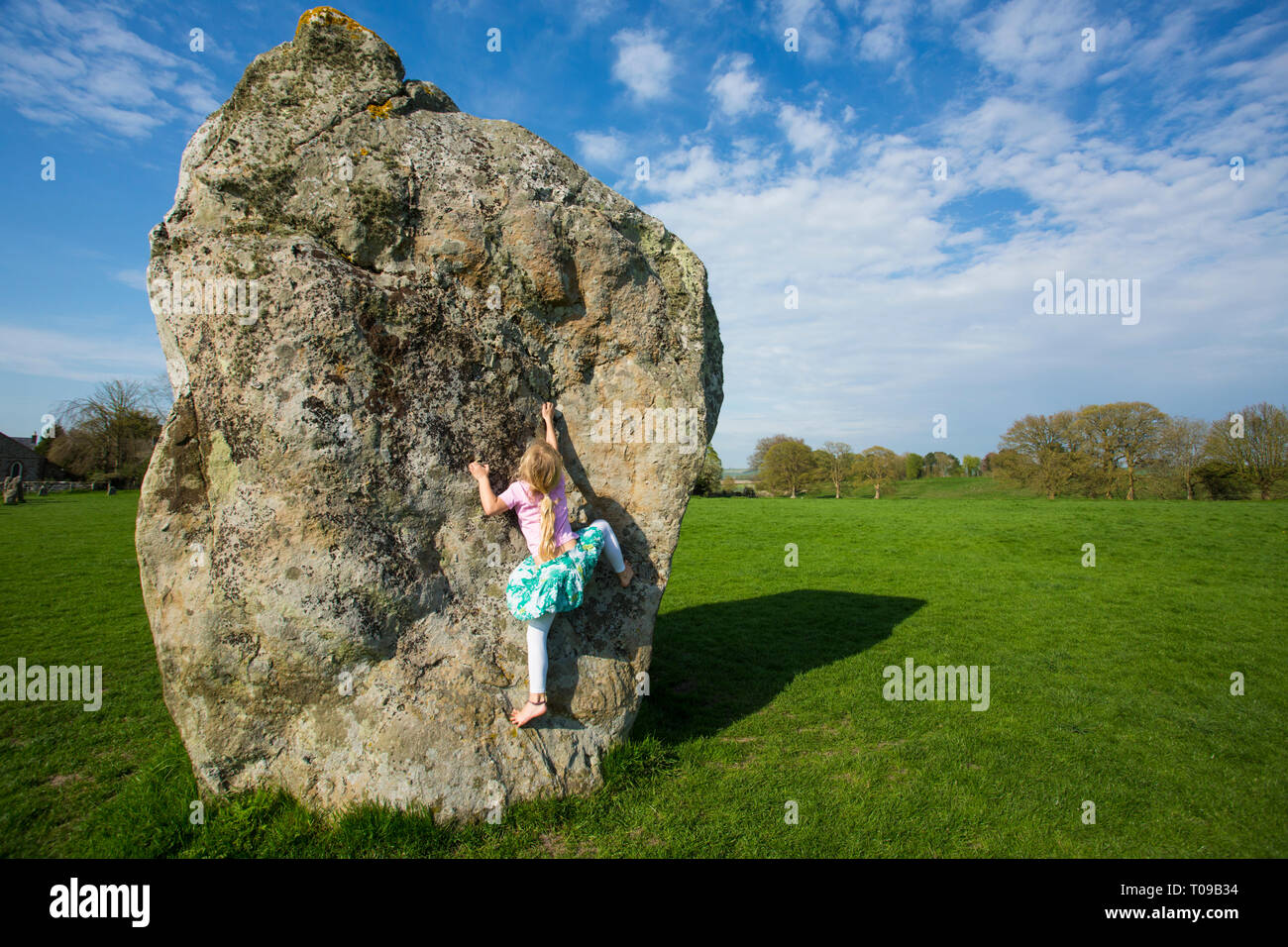 Great Britain, England, Avebury Stone Circle. Young girl climbing a huge Neolithic megalith. MR. Stock Photo