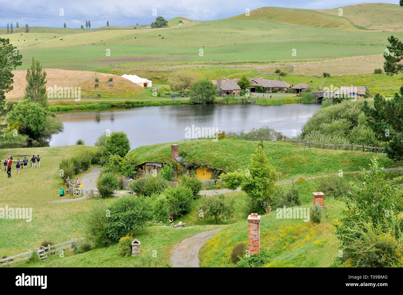 Hobbiton movie set in the Waikato region of New Zealand north island. Rolling hills of The Shire with lake, mill, bridge, Green Dragon Inn. Visitors Stock Photo
