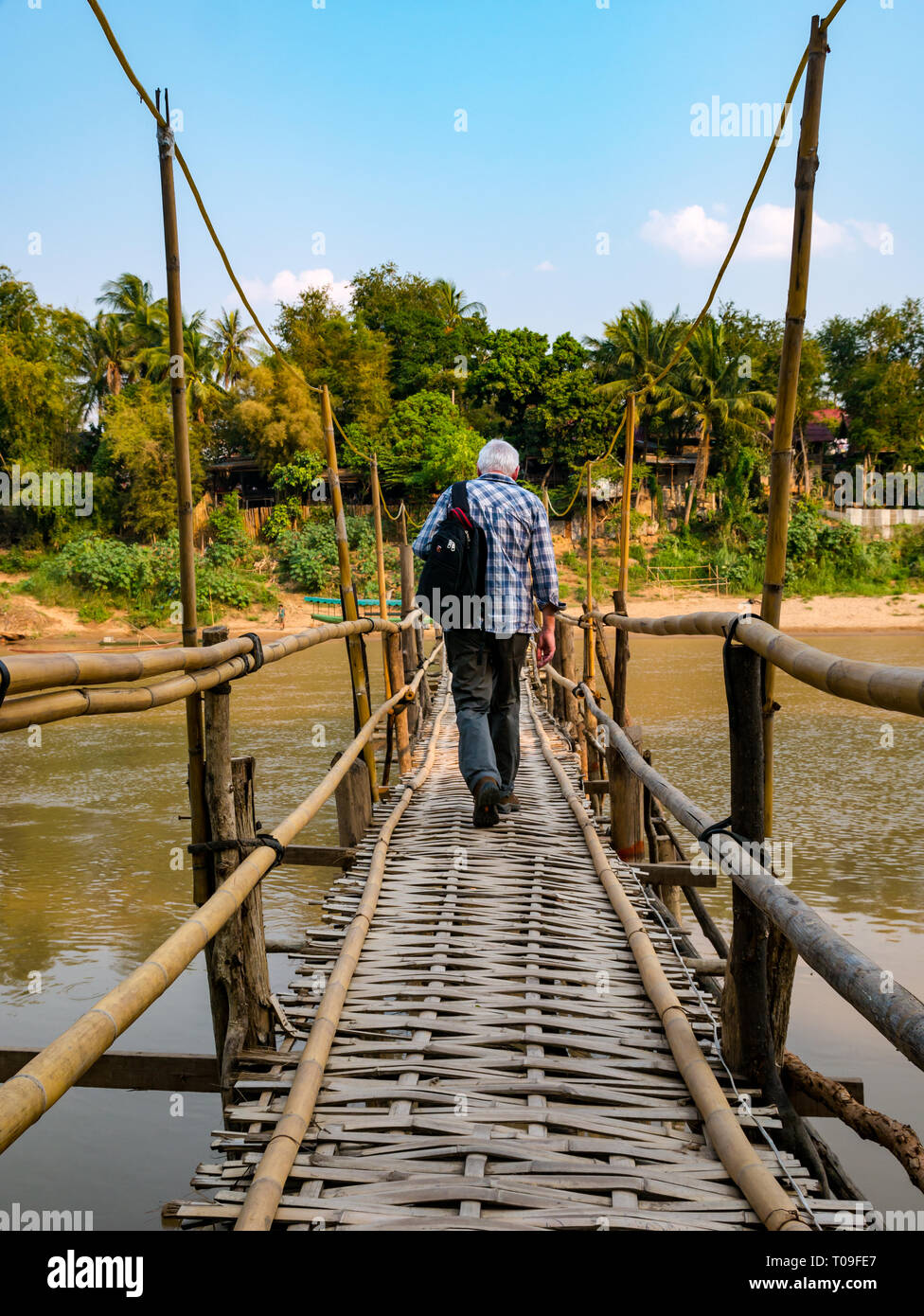 Senior male tourist walking across rickety bamboo cane bridge over Nam Kahn river tributary of Mekong, Luang Prabang, Laos, Indochina, SE Asia Stock Photo
