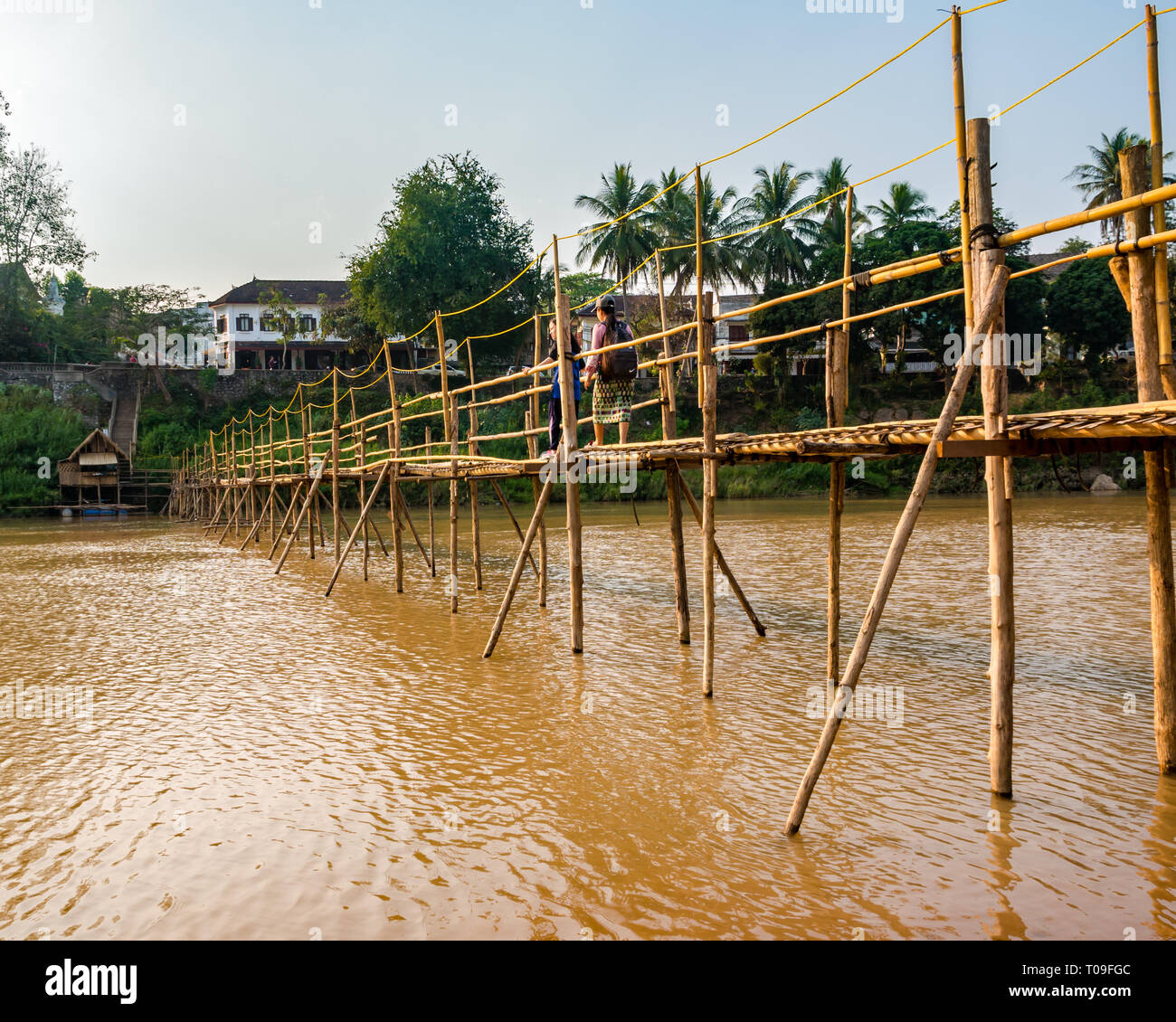 Girls walking across rickety bamboo cane bridge over Nam Kahn river tributary of Mekong, Luang Prabang, Laos, Indochina, SE Asia Stock Photo