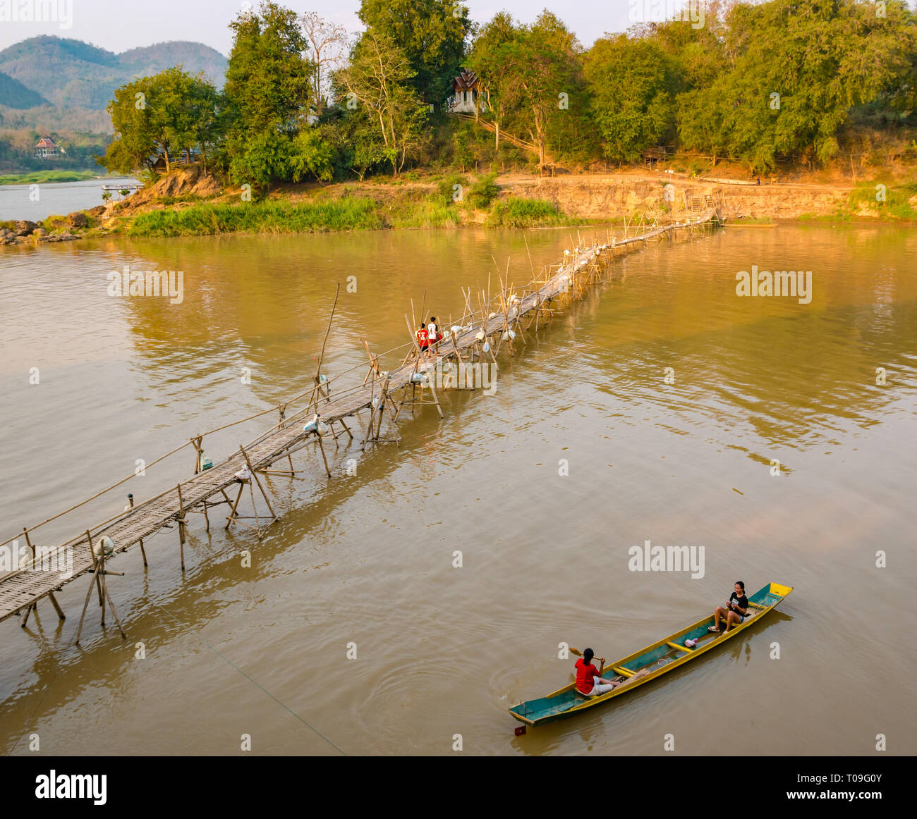 Boys walking on rickety bamboo cane bridge with girls in dugout canoe, Nam Kahn river tributary of Mekong, Luang Prabang, Laos, Indochina, SE Asia Stock Photo