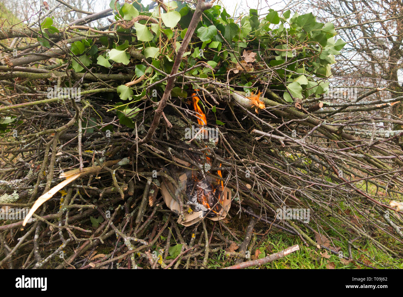 Setting fire with paper and cardboard to light a domestic bonfire to burn leaves, tree branches & twigs, lit in a domestic garden in the countryside. (104) Stock Photo