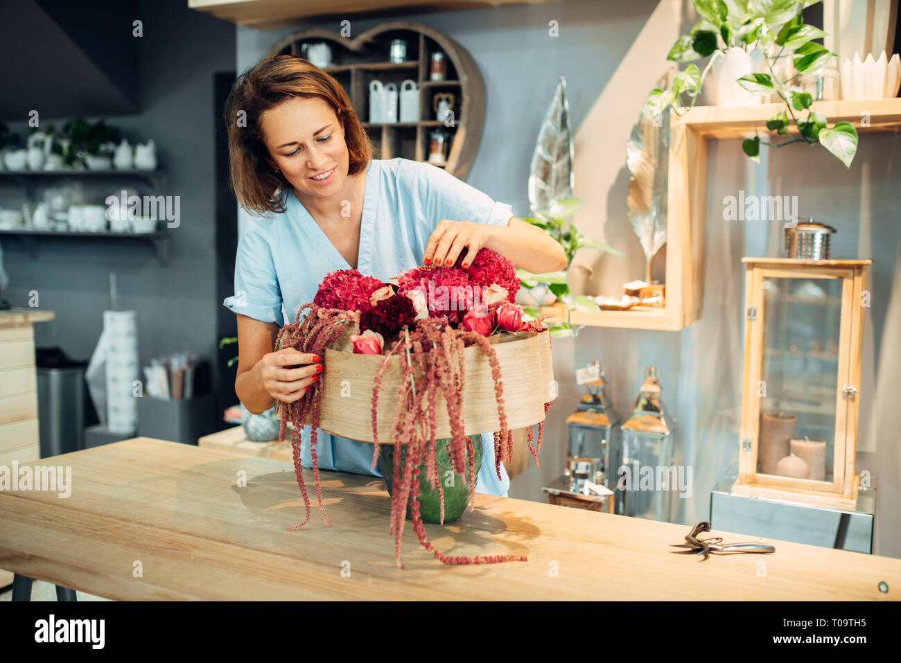 Female florist decorates frsh bouquet of flowers in shop. Floral artist making composition at the workplace. Floristry service Stock Photo