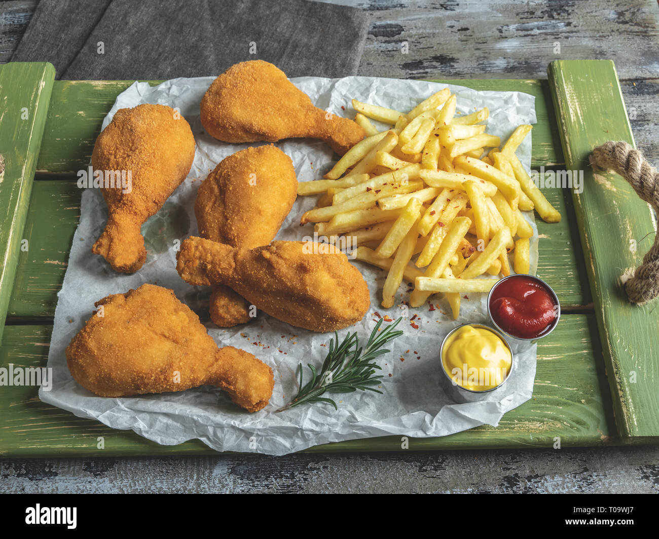 crispy fried chicken legs breaded golden color, french fries, sauce, wooden background Stock Photo