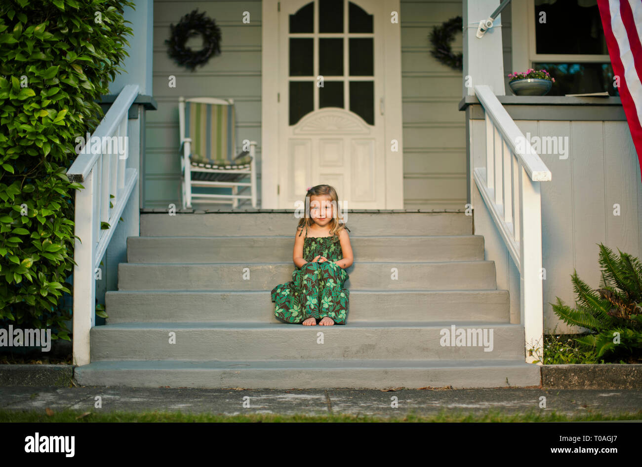 Portrait of a happy young girl sitting on the front steps of a suburban house. Stock Photo